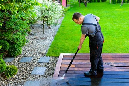 A professional cleaner washing wooden deck in a garden with pressure washer in Essex UK