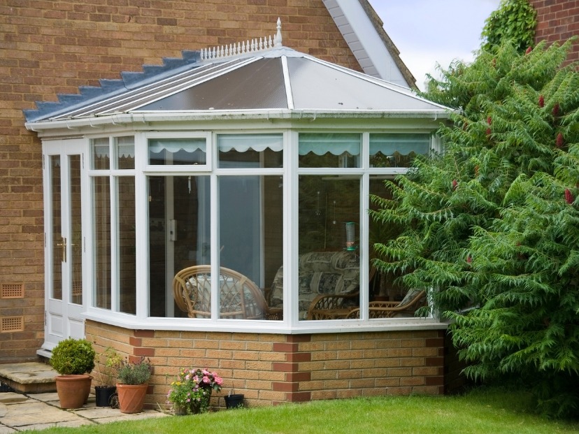 the picture is showing a cleaned Conservatory with glass walls wooden furniture and outside with flower pots grass and tree in Essex Uk