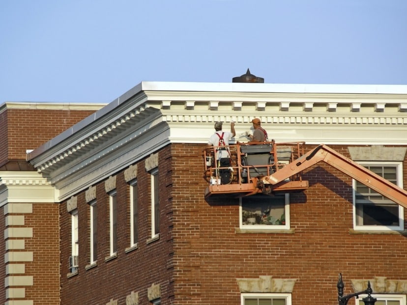 Two Painters on a cherry picker, elevated high above the ground, painting exterior of a building In Essex England UK