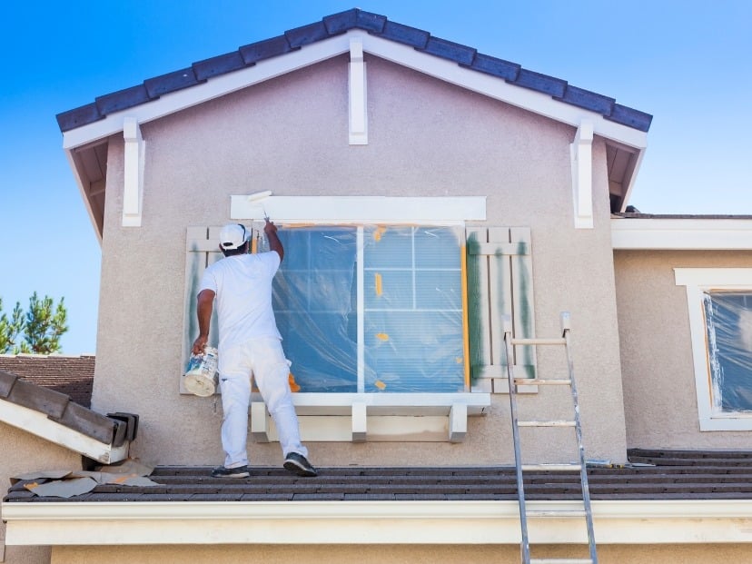 A worker carefully painting the window frame of a house with a brush, focusing on precision and detail in Essex county England UK