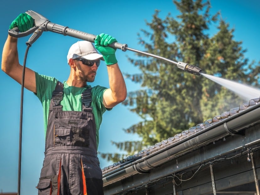 home and Garden Masters worker wearing glasses cleaning roof with pressure washer somewhere in Essex County England UK