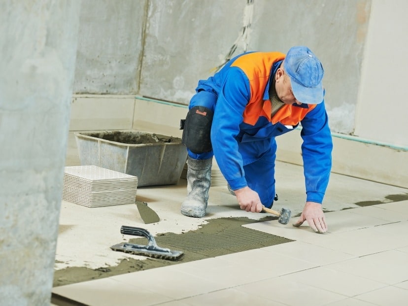 A worker skillfully laying tiles on a floor, creating a neat and precise pattern with his tools and expertise In Essex UK