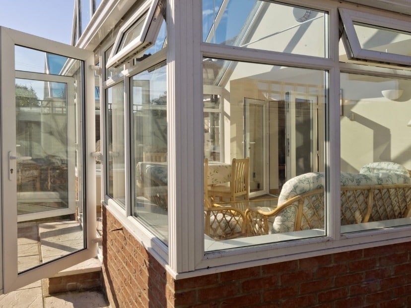 With Glass walls cleaned Conservatory with wooden furniture and Open glass doors In Essex county England UK